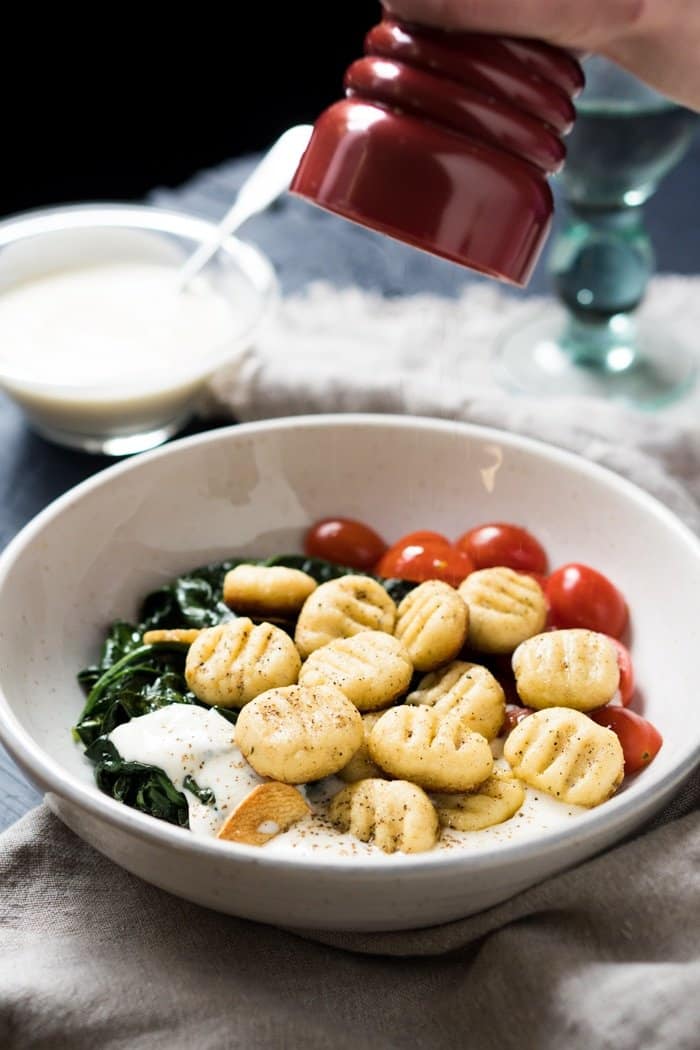 Freshly grinding black pepper onto a plate of keto ricotta gnocchi