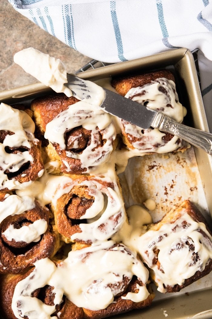 Smearing glaze on keto cinnamon rolls in gold baking pan