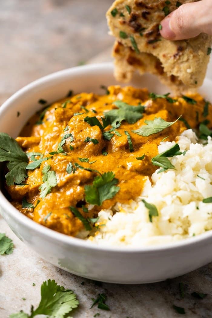 Dipping keto naan into a butter chicken bowl