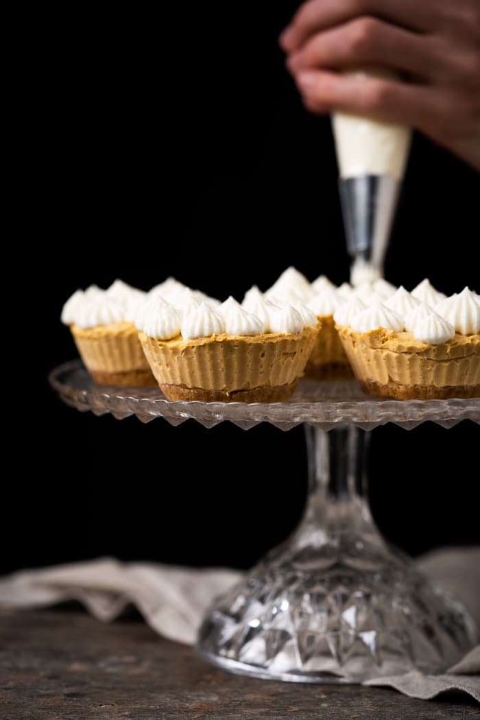 Piping whipped cream on top of mini keto pumpkin cheesecakes