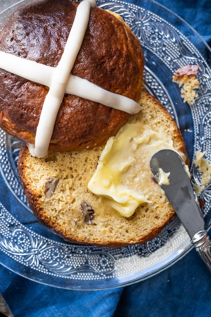 Smearing butter on a halved gluten free hot cross bun