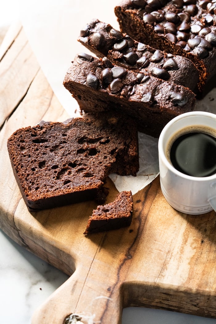 Closeup slice of Keto chocolate zucchini bread on a wooden board with coffee on the side