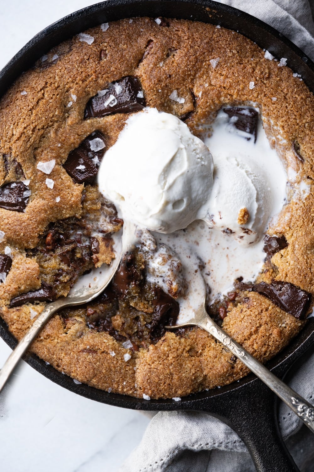 Two spoons eating gooey chocolate keto skillet cookie with melting vanilla ice cream