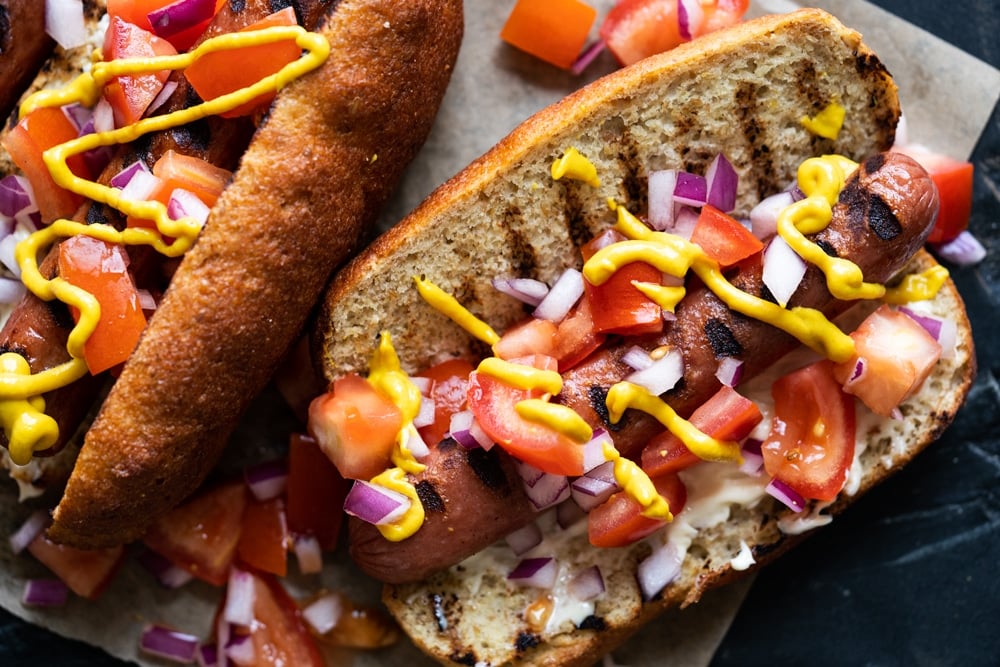 Closeup of a keto hot dog with a fluffy yeast buns, pico de gallo salsa and a drizzle of mustard