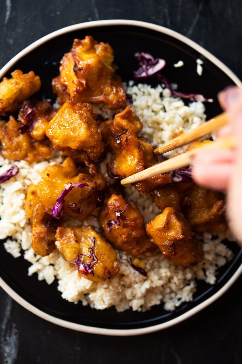 Taking a piece of keto orange chicken with a chop stick