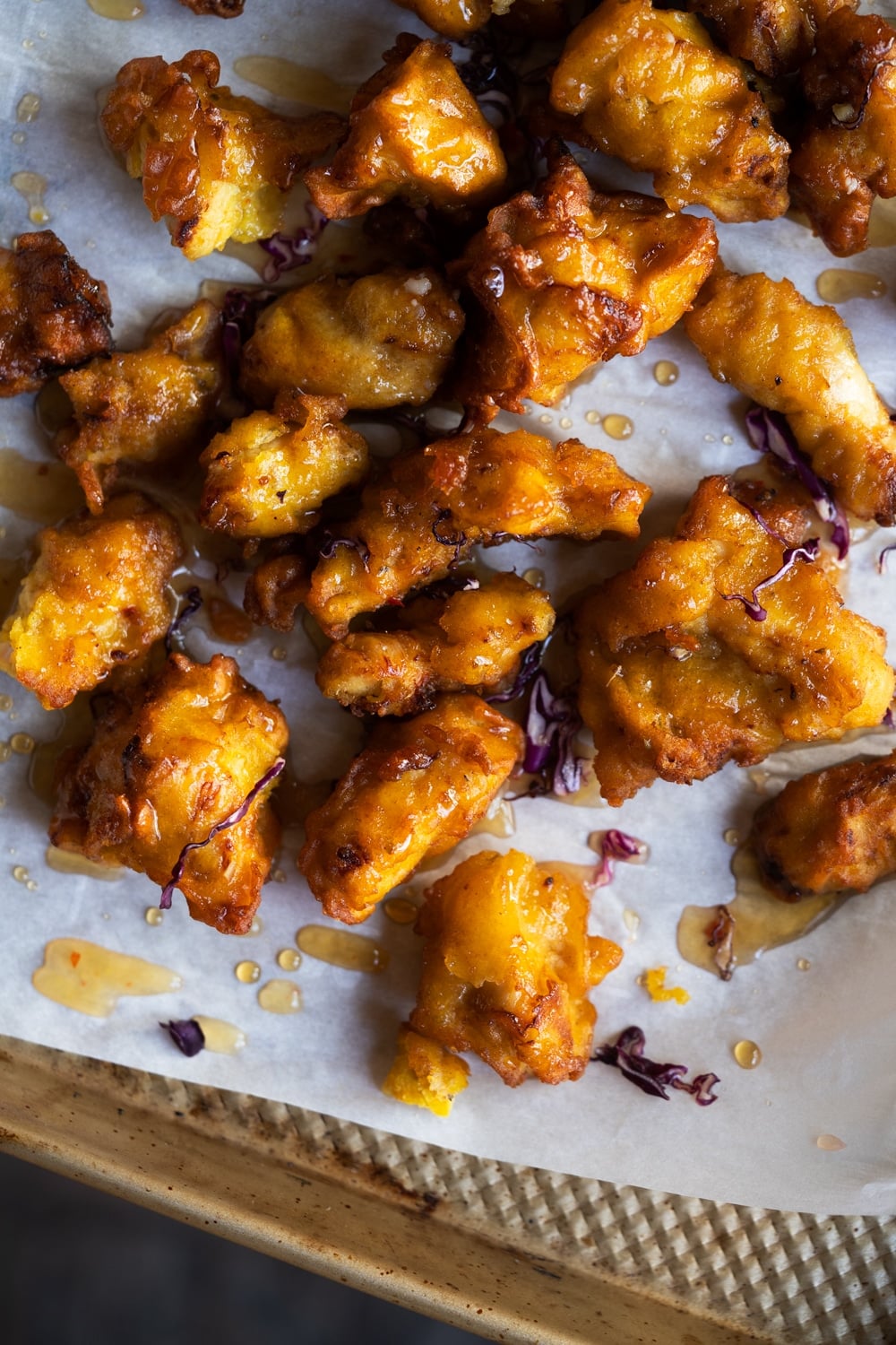 Mixing the fried battered chicken bites with the orange glaze on a baking tray