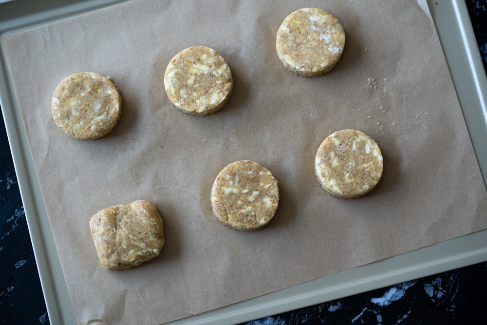 Overhead shot of six unbaked keto shortcakes on a baking tray with parchment paper