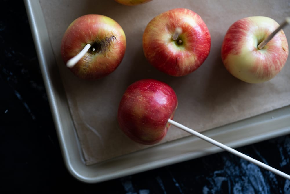 Skewered red apples on a gold baking tray with parchment paper