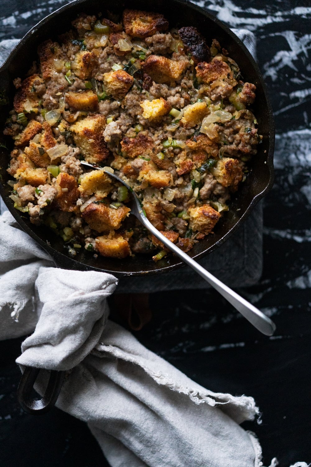Serving keto cornbread stuffing from a black skillet, with the handle wrapped in linen cloth