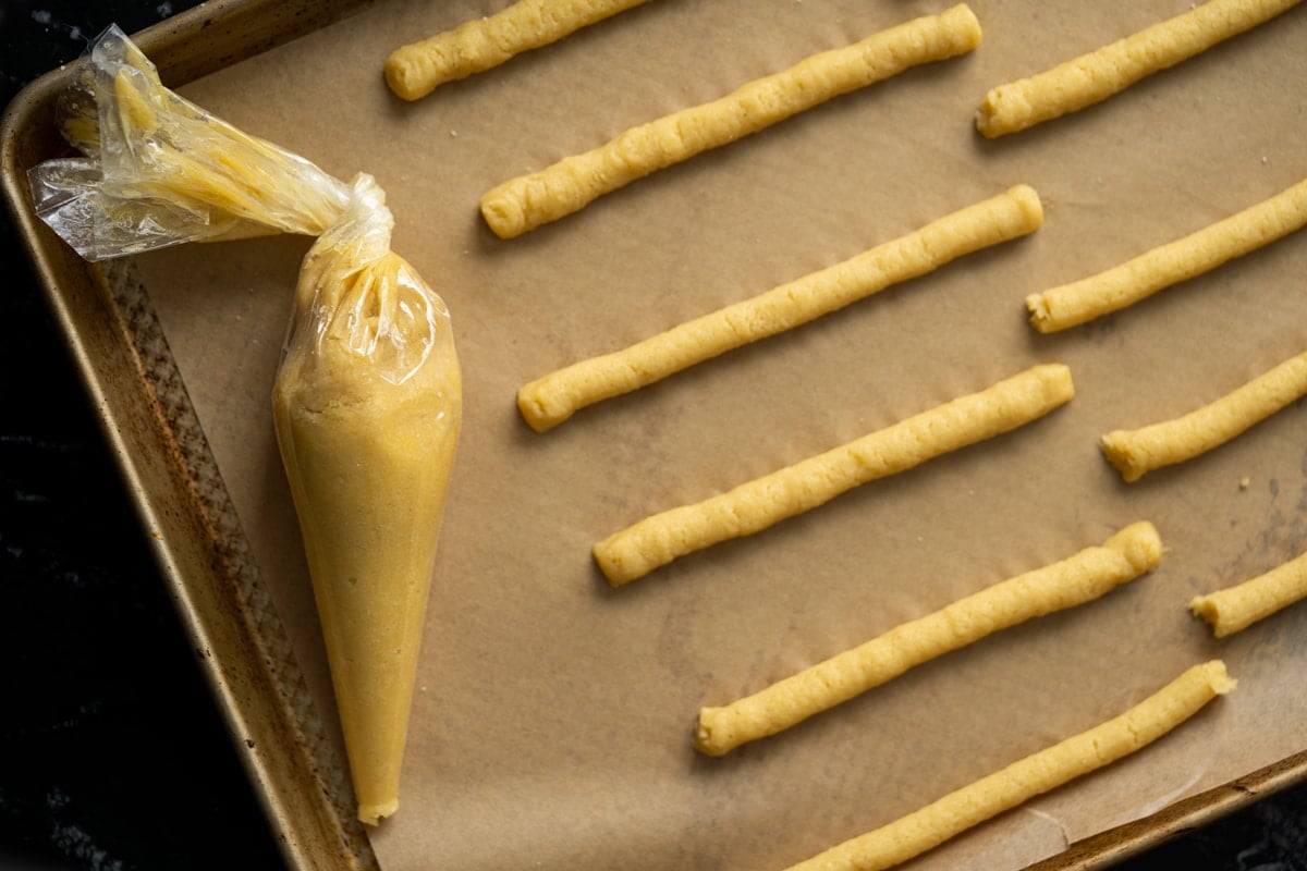 Piping out the keto breadsticks onto a baking tray with parchment paper