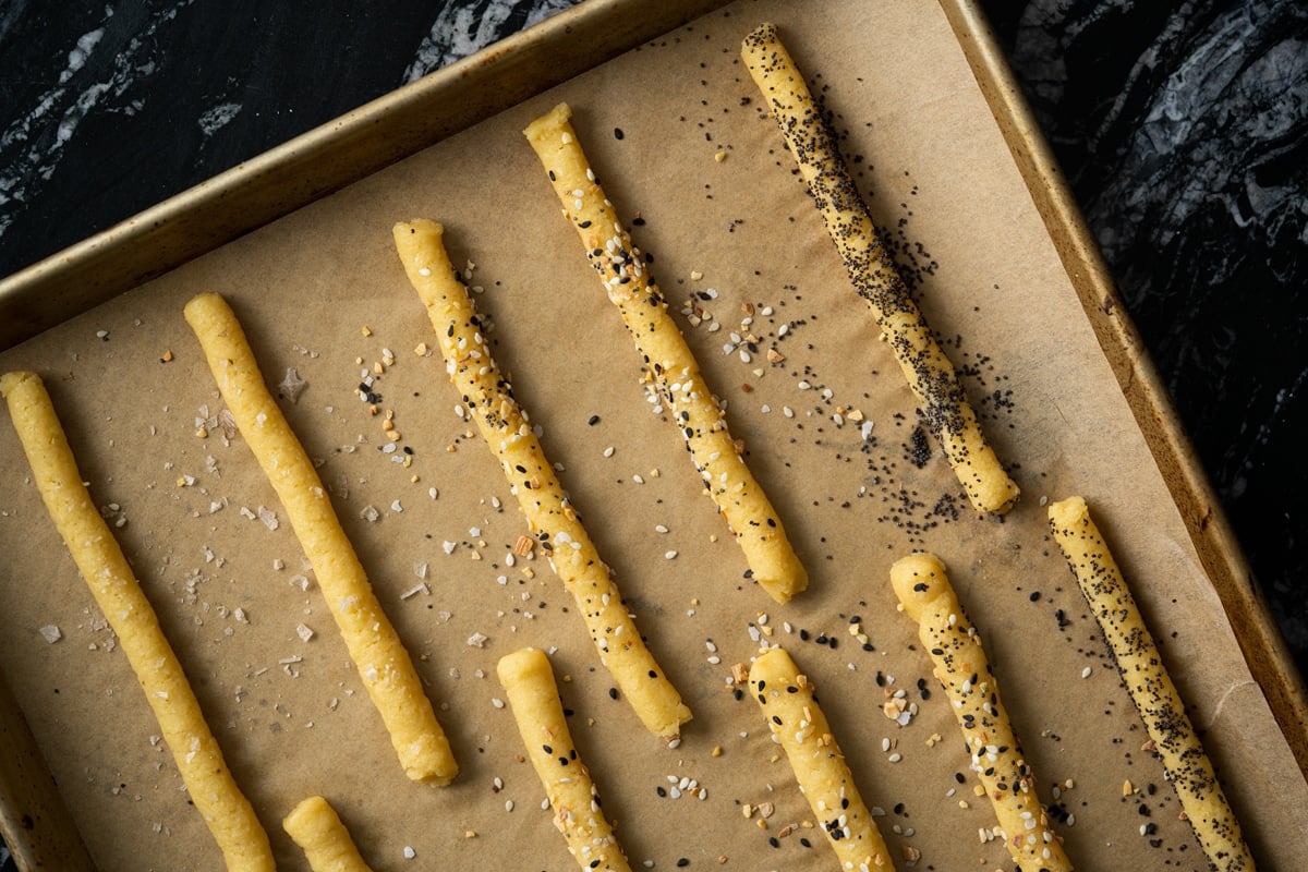 Sprinkling various toppings onto the unbaked keto breadsticks