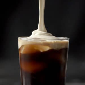 Pouring the salted caramel cream onto a tall glass with cold brew and ice