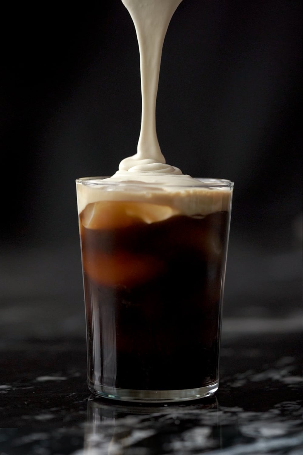 Pouring the salted caramel cream onto a tall glass with cold brew and ice