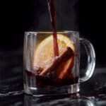Pouring a refined sugar free keto mulled wine onto a glass mug with an orange slice and cinnamon stick