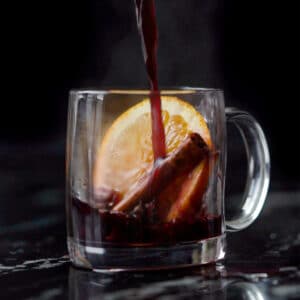 Pouring a refined sugar free keto mulled wine onto a glass mug with an orange slice and cinnamon stick