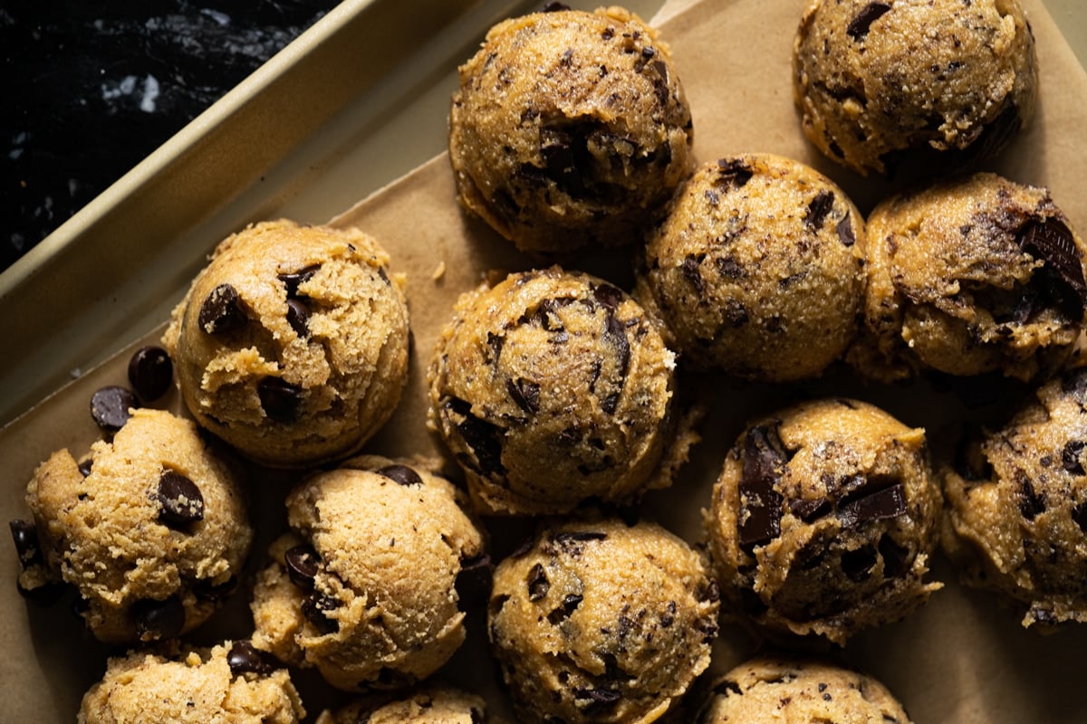 Closeup keto cookie dough with chocolate chips scooped out onto a baking sheet