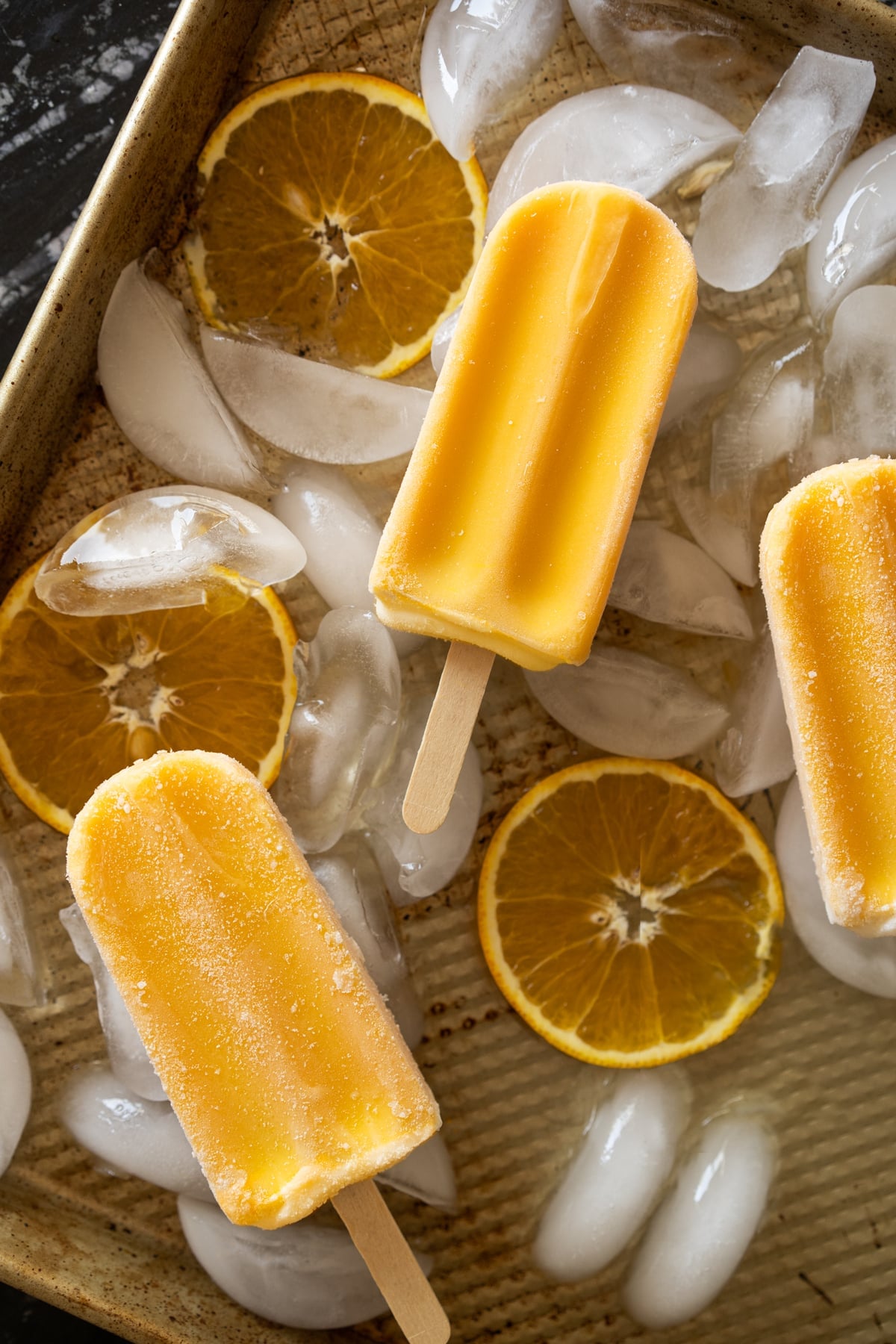 Keto orange creamsicle popsicles on a baking tray with ice