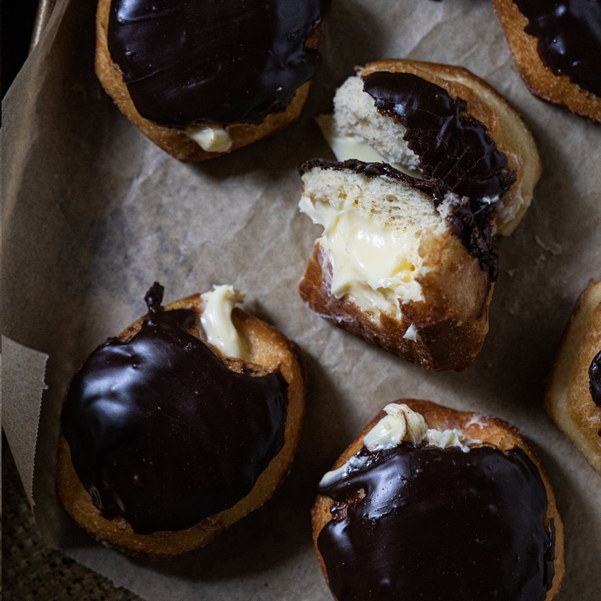 Keto boston cream donuts with a chocolate glaze and custard filling freshly baked on a baking tray