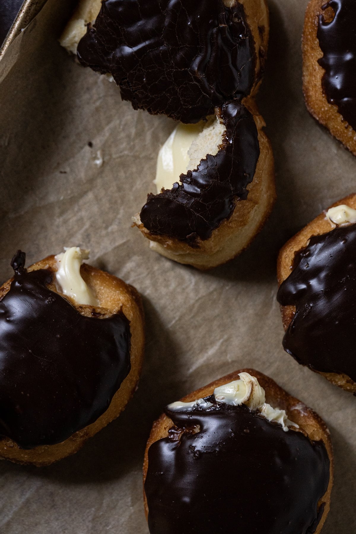Keto boston cream donuts with a chocolate glaze and custard filling on a baking tray