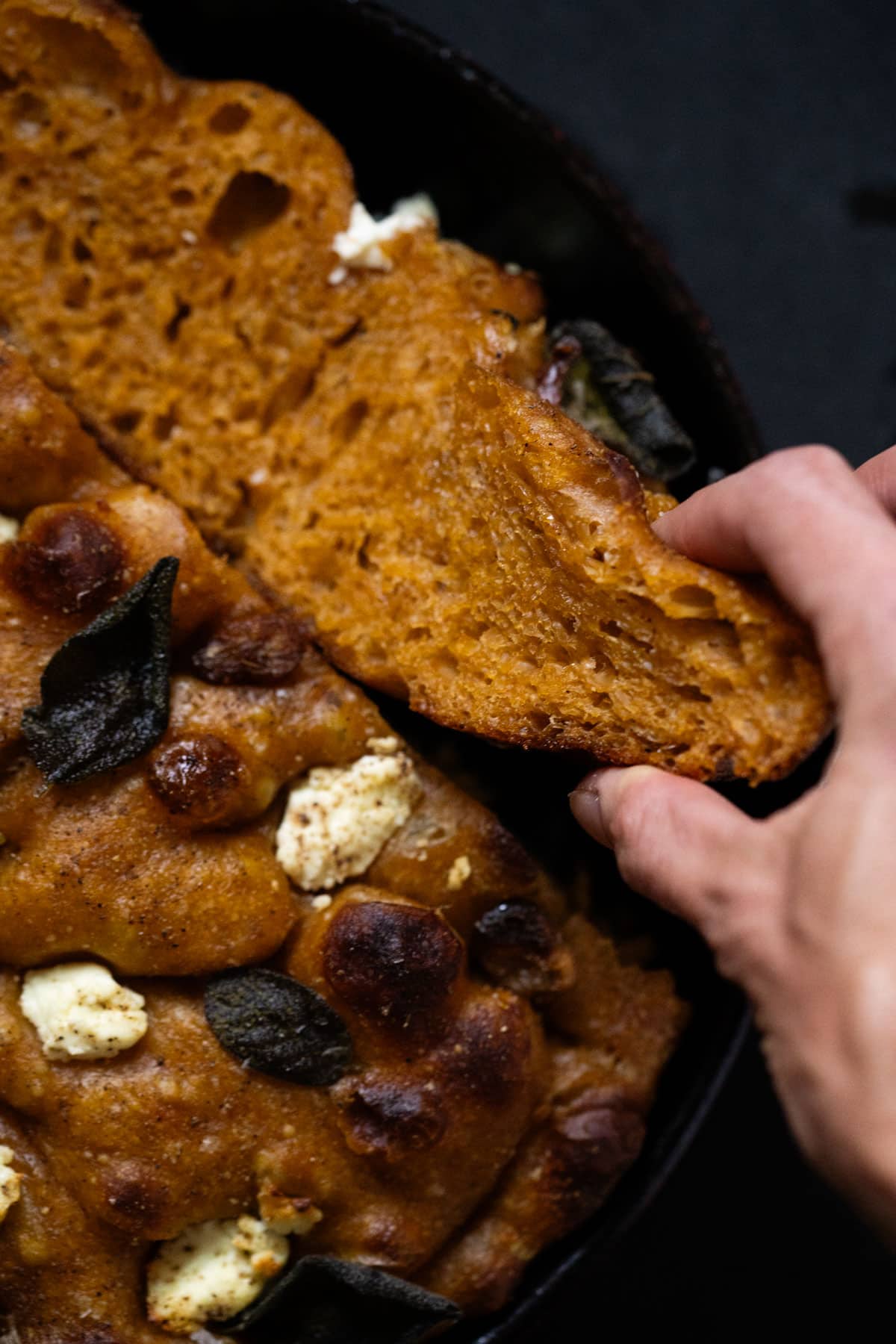Taking a slice of freshly baked sourdough pumpkin focaccia showing the plush crumb and crisp exterior