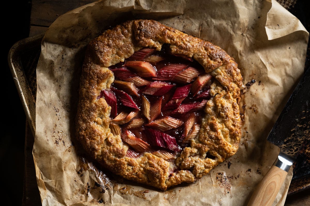 Freshly baked strawberry rhubarb galette on a baking tray with a knife